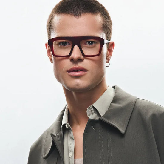 Jeune homme portant de grandes lunettes rectangulaires rouges lors d’un examen de la vue à Laval, en gros plan sur le visage.